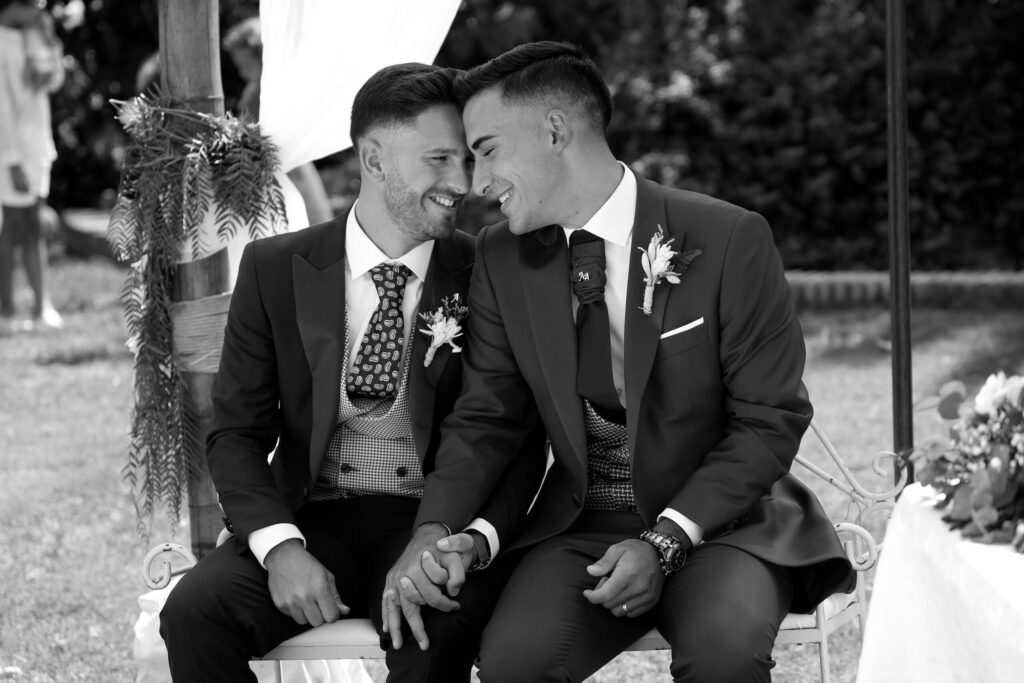 Dos novios sentados de la mano durante su ceremonia, fotografía en blanco y negro de Gustavo Valverde