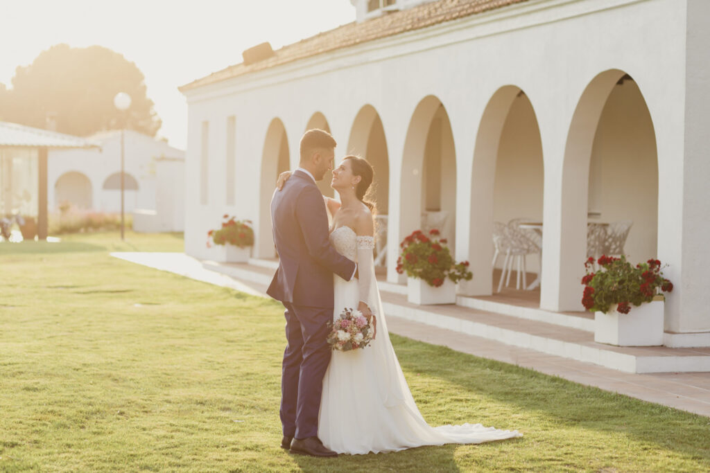 Novios abrazados junto a una galería de arcos al atardecer, fotografía de AL Fotografía