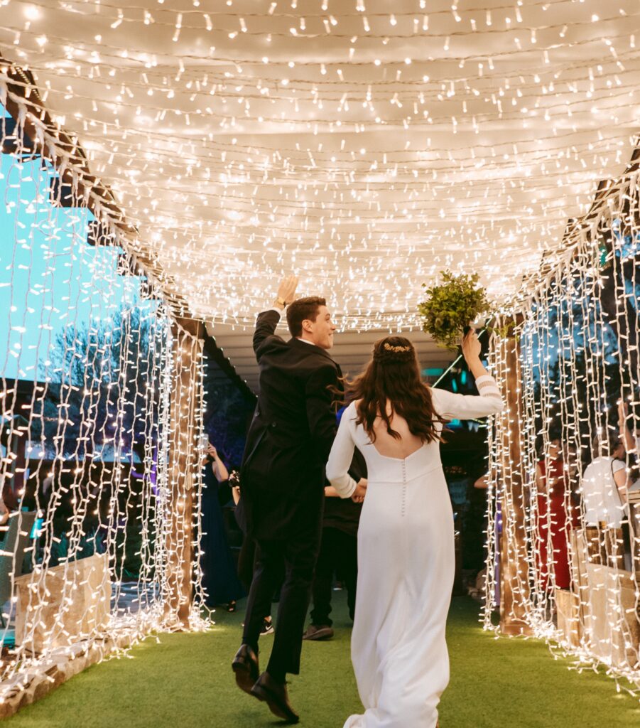 Pareja entrando a la celebración bajo iluminación decorativa diseñada por azulymalva