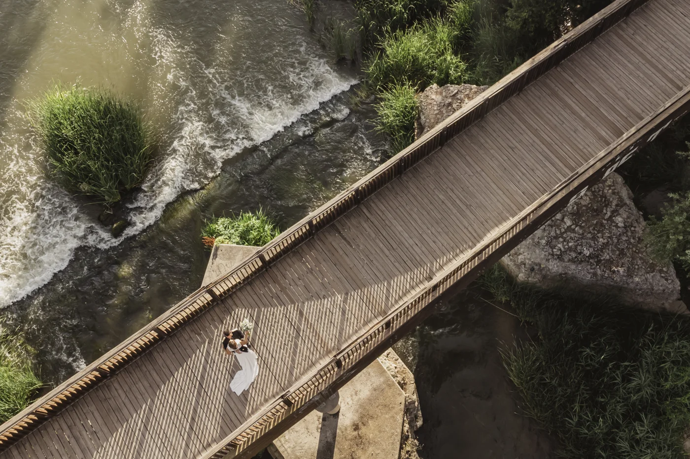 Pareja de novios sobre un puente de madera junto al río, fotografiada desde arriba por AL Fotografía