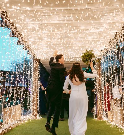 Pareja entrando a la celebración bajo iluminación decorativa diseñada por azulymalva